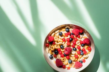 Yeşil zemine izole edilmiş taneli ve meyveli nefis sağlıklı kahvaltı. Yoğurtlu müsli. Bol meyveli müsli kahvaltı.