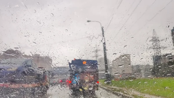 El fondo está borroso, gotas de lluvia en el parabrisas para el coche. Gotas de agua en la superficie de vidrio en la carretera. Desenfoque, bokeh y luces de la calle behind.heavy camino lluvioso y resbaladizo. Resumen coche mal tiempo — Foto de Stock