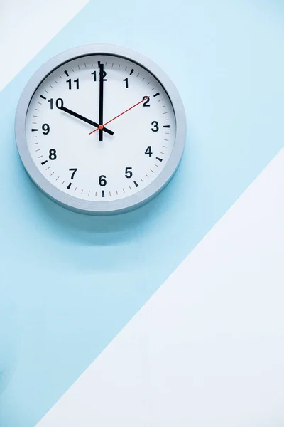 简约的白色挂钟，蓝白色背景上有浅色金属。时间概念工作时间的主题工作时间的概念正在进行中。几何背景。时间不多了 — 图库照片