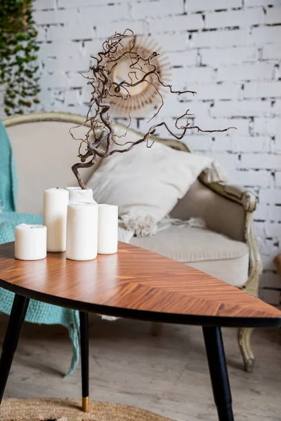 Witte kaarsen op houten salontafel in gezellige woonkamer interieur.Stijlvolle Scandinavische huiskamer.Kaars en plant in vaas op kleine houten tafel voor Scandinavisch ontworpen bank. boho huis — Stockfoto