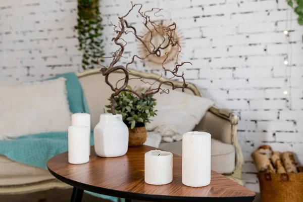 Witte kaarsen op houten salontafel in gezellige woonkamer interieur.Stijlvolle Scandinavische huiskamer.Kaars en plant in vaas op kleine houten tafel voor Scandinavisch ontworpen bank. boho huis — Stockfoto