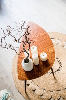 wooden small table with ceramic vase with branches on a round straw carpet. boho interior.Natural eco home decor.Hygge scandinavian style concept.cozy living room.Top view