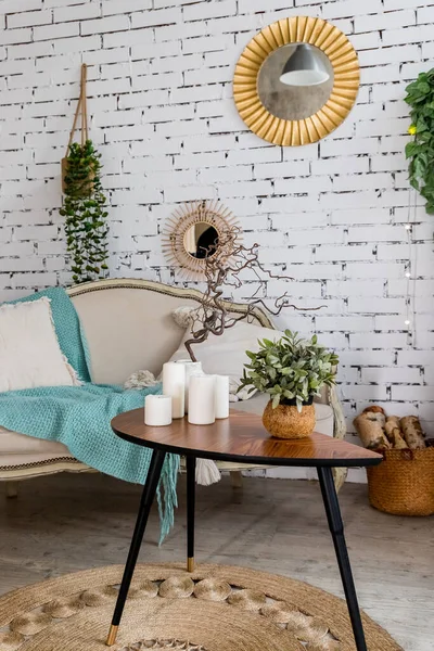 Beige en textuur kussens op beige bank, muntdeken. Kleine tafel met kaarsen. Stijlvol Scandinavisch interieur van woonkamer met bank, kussens, elegante persoonlijke accessoires en planten op bakstenen muur. — Stockfoto