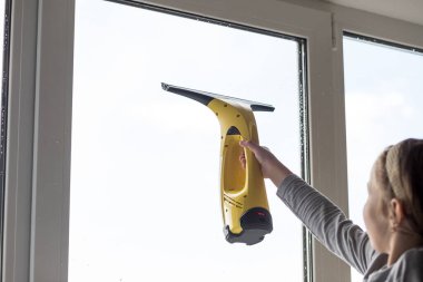 Küçük kız oturma odasındaki büyük pencereyi portatif elektrikli süpürgeyle yıkıyor. Kız evde cam siliyor. Çocuklar evde yardım eder. Ebeveynlerin ev temizliğine yardım etmek. Çocukların camları silmesi.