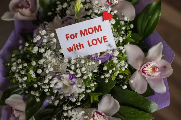 Ramo de orquídeas, Lisianthus, Gypsophila y corazón con texto para mamá con amor. El día de las madres. Un regalo para mamá para el Día Internacional de la Mujer, o birthday.message con corazón rojo —  Fotos de Stock