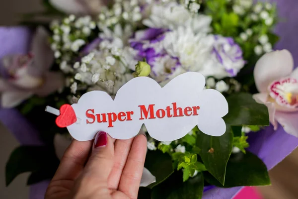 Flores de orquídea y regalo floral para mamá. El concepto de Feliz Día de las Madres. Mensaje en mano femenina, super madre.Sábana blanca con corazón rojo y texto super mamá . —  Fotos de Stock