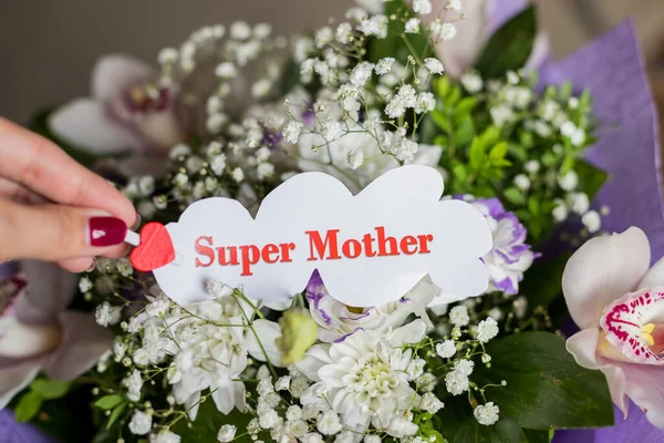 Fiori del Orchid e regalo floreale per il mom. Il concetto di Happy Mothers Day. Messaggio in mano femminile, super mother.White foglio con cuore rosso e super mamma testo . — Foto Stock