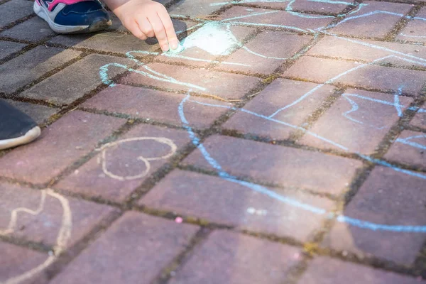 Девушка сидит на бетонной асфальтовой дороге., на каменной дорожке. Дети рисуют линии, цифры мелом на асфальте. Маленькая девочка рисует на тротуаре цветным шалфеем . — стоковое фото
