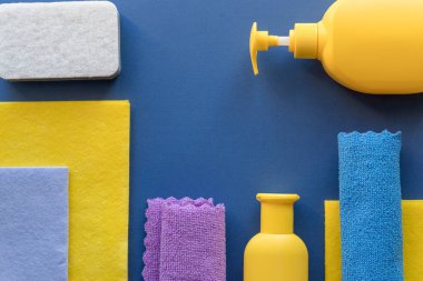 Mavi arka planda farklı yüzeyler için renkli temizlik seti. Tedarikçilerle temizlik konsepti. Plastik şişeler, deterjan kapları, mikrofiber bez, sünger. Paçavra ve deterjan.