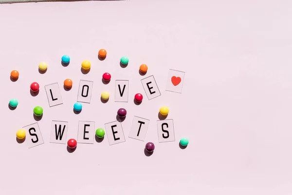 Ассортимент сладких конфет на розовом фоне .colorful конфеты и текст любят sweets.Flat лежать композицию с желе бобы. Цветные шоколад candies.chocolate кнопки — стоковое фото