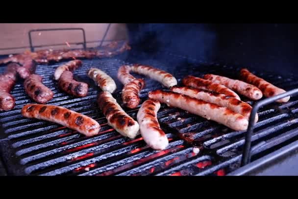 Bratwurstgrillen aus nächster Nähe. Bereiten Sie ein paar Würstchen und Hot Dogs auf dem flammenden Holzkohlegrill zu. Klassisches Essen zum Mitnehmen. Streetfood auf Herdplatte gekocht. — Stockvideo