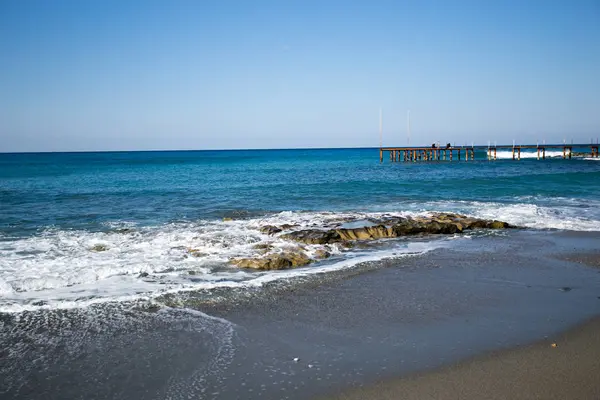 Praia de areia com mar azul e algumas rochas na água — Fotografia de Stock