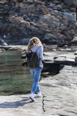 Sarışın kadın turist kayanın üzerinde yürüyen sırt çantası ile kıyı yivli