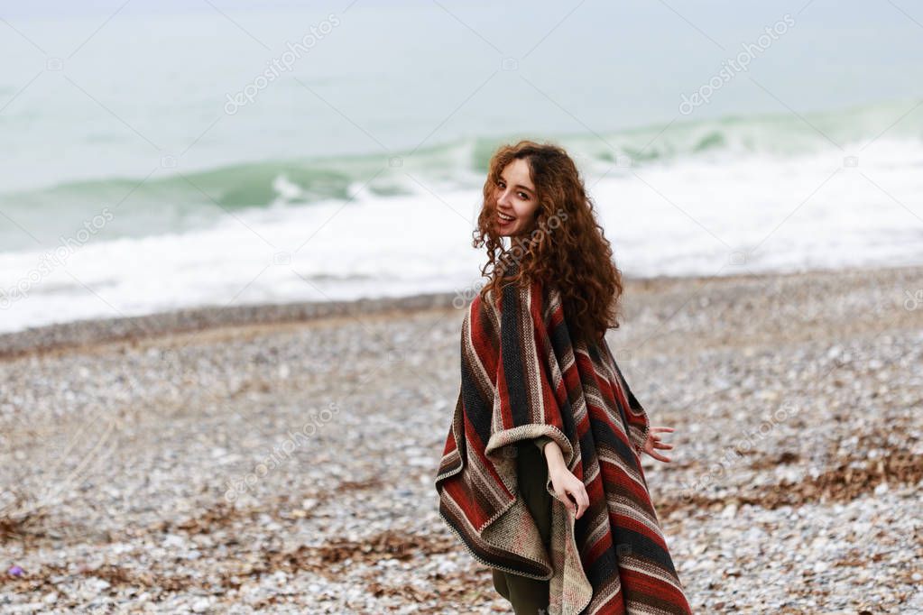 Portrait of happy brunette woman on the beach wearing poncho 