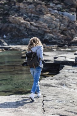 Sarışın kadın turist kayanın üzerinde yürüyen sırt çantası ile kıyı yivli