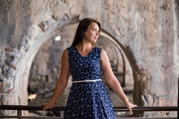 Jovem mulher em vestido azul escuro na frente de arcos de pedra olhando — Fotografia de Stock