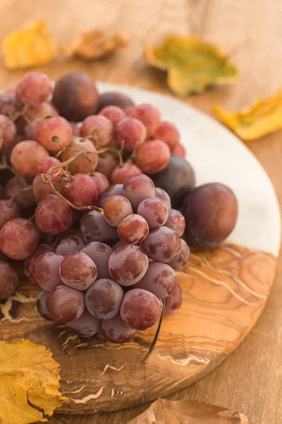 Виноград и сливы на полу-деревянной полумраморной тарелке — стоковое фото