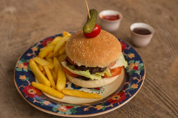 Hamburger with french fries in plate with ornaments — Stock Photo, Image