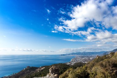 Ön planda antik kentin kalıntıları ve uzak görüşte kentsel peyzaj ile dağlar ile Akdeniz manzara.