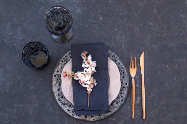 Çiçek açan badem dalı ve bakır renkli çatal bıçak takımı ile siyah, gri ve pembe renklerde bahar masa ayarı