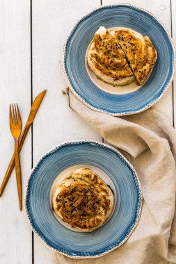 Beyaz ahşap masa üzerinde bakır renkli çatal bıçak takımı ile iki mavi kremsi tabakta türk pasta borek topview çekim.