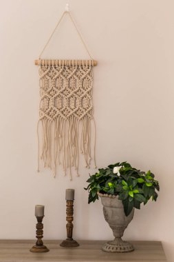 İç dekorasyon konsepti. Macrame duvar sanatı, ahşap mumluklar ve metal vazo gardenya çiçeği. Dikey kompozisyon.