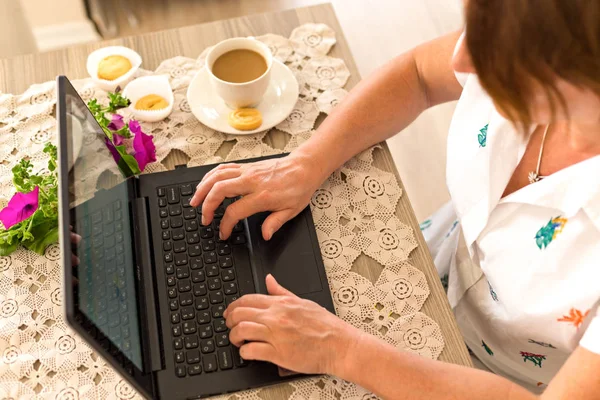 Spring or summer freelance or home office concept. Woman wearing white shirt, working from her home office with laptop located on table covered by lace tabletop.