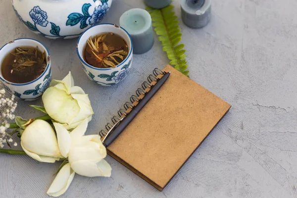 Free writing concept. Styled feminine work desk with notepad, herbal tea and roses on concrete tabletop.