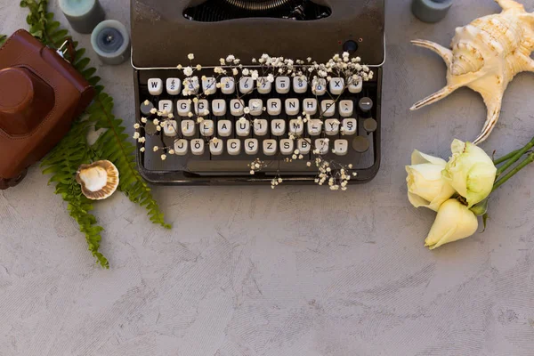 Summer or spring writing and freelance concept. Styped topview  photo of vintage typewriter with roses, leather vintage camera and seashell. Copy space. Horizontal composition.