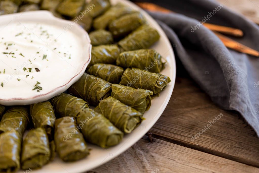Stuffed grape leaves dolma on round platewith yogurt in the center of the plate.