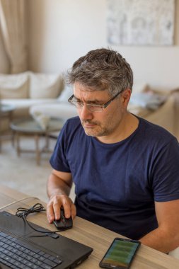Orta yaşlı bir adam laptopunu kullanarak evden çalışıyor.
