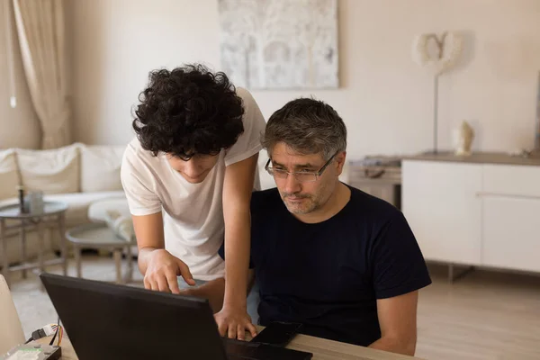 Papa et fils étudient de la maison ensemble en utilisant un ordinateur portable noir — Photo