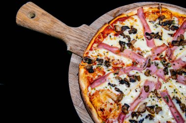 Ahşap tabakta servis edilen yeni pişmiş jambon ve mantarlı pizzanın yakın çekimi. 