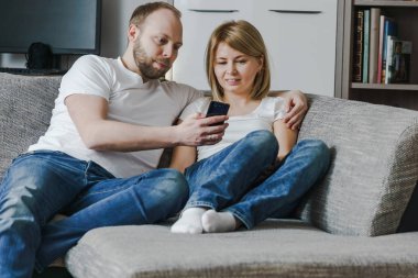 Doğal, yaşam tarzı çekici çift birlikte bakarak smartphone oturma odasında kanepede oturan görüntüsünü.