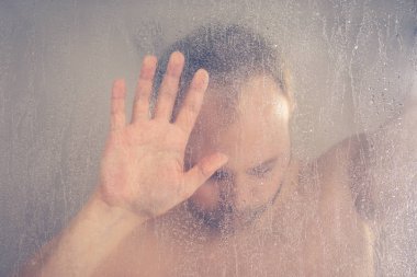 su akan ve duşakabin banyo şeffaf buğulu cam kapının arkasında kafasını tutarak altında ayakta duş alırken adam vurguladı