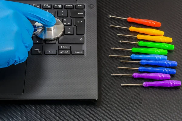 kişi el tanı laptop Tornavidalar gökkuşağı koleksiyonu ile karbon zemin üzerine stetoskop ile