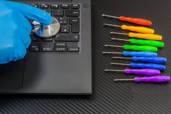 person hands diagnostic laptop with stethoscope on carbon background with rainbow collection of screwdrivers