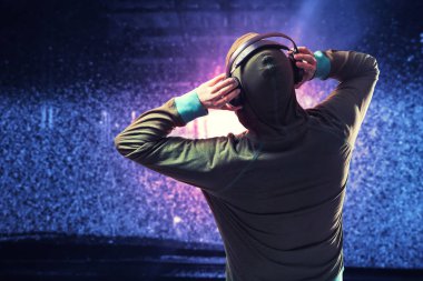 Bir hoodie gömlekli bir adam siluet su damlaları ile bulanık mavi ve kırmızı zemin üzerine siyah kulaklık aracılığıyla müzik dinler.
