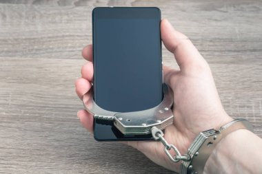Kişiyi rehin gadget tarafından insanlar. Erkek eli ile bağlı kelepçe cep telefonu, sıcak tonlama mat.