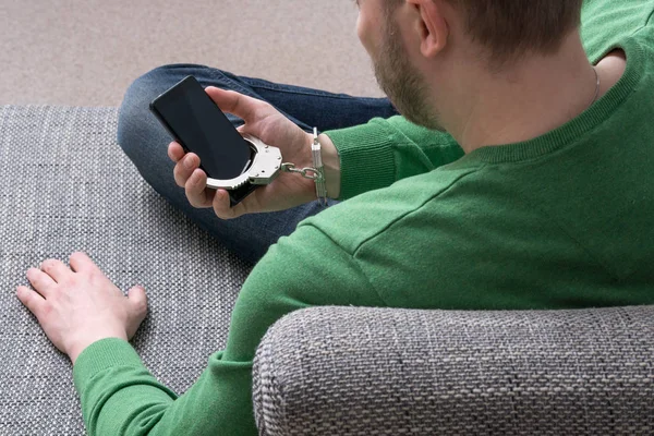 Kişiyi rehin gadget tarafından insanlar. Bir kanepe ve elini kelepçe ile cep telefonunuza bağlı oturan adam