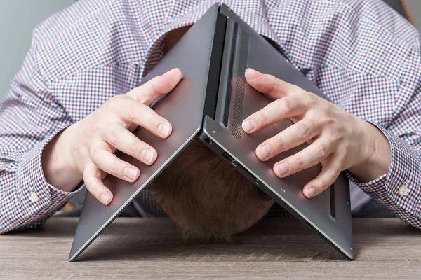 Stressed young man covering his head with his laptop. Burn out at work concept.