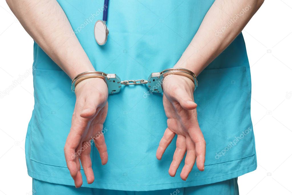 Yung doctor in blue uniform with stethoscope attached to handcuffed at the wrist on the white background.