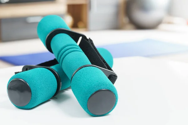 Fitness at home concept, a pair of green dumbbells in the foreground and an fitness ball and exercise mat in the background in fitness in living room.