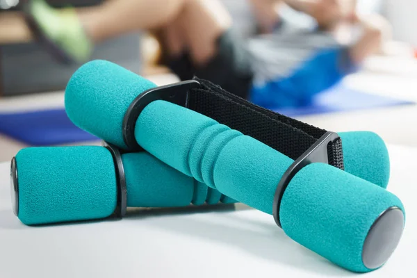 Fitness at home, a pair of green dumbbells in the foreground and man doing sit ups on exercise mat in the background in fitness in living room.