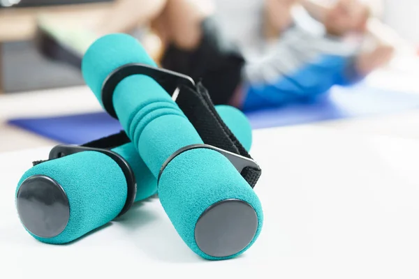 Fitness at home, green dumbbells in the foreground and man doing sit ups on exercise mat in the background in fitness in living room.