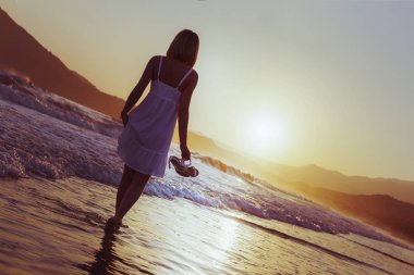 Bir kız Crete ada kıyı şeridinde günbatımı zamanda yürüyor.