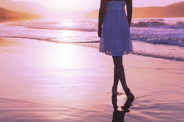 A girl is walking along Crete island coastline at the sunset time, lilac toning. — Stock Photo, Image