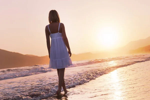 Bir kız Crete ada kıyı şeridinde günbatımı zamanda yürüyor. Sıcak tonlama.