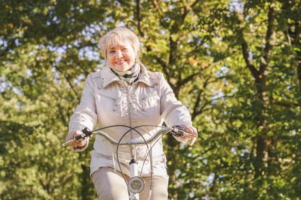 Ativo feliz despreocupado sorrindo sênior mulher livrando bicicleta no outono natureza . Imagem De Stock