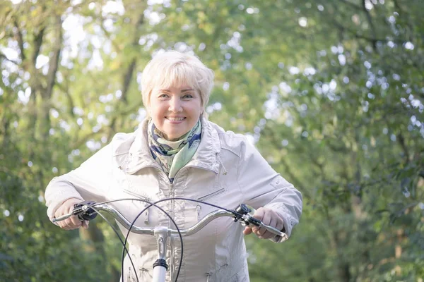 Ativo feliz despreocupado sorrindo sênior mulher livrando bicicleta no outono natureza . Imagem De Stock